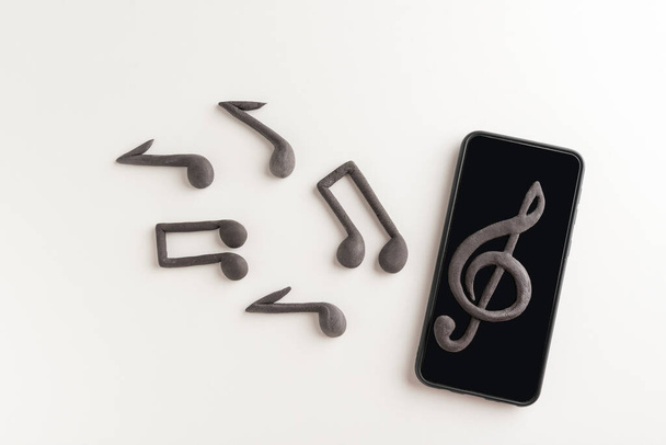 Teléfono inteligente con clave triple en pantalla y notas musicales sobre fondo blanco. Aplicaciones para escuchar música en tu teléfono - Foto, imagen