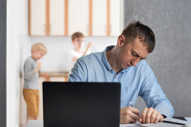 Mladý muž se snaží soustředit na práci, zatímco děti dělají hluk. Práce doma, na volné noze, práce na dálku.  - Fotografie, Obrázek