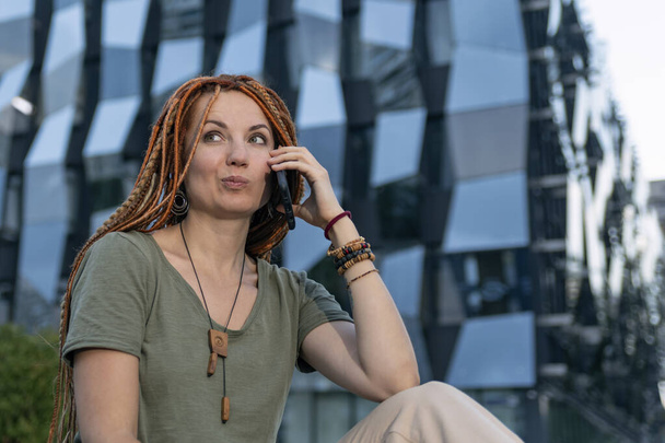 Beautiful girl with red dreadlocks was surprised by the phone call. Invitation to an interview. Non-standard employee. Unexpected call - Photo, Image
