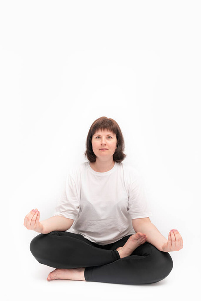 Retrato de mujer caucásica de talla grande sobre fondo blanco practicando yoga. Ardha-padmasana, media pose de loto. Enmarcador vertical. Copiar espacio. - Foto, Imagen