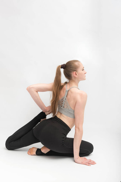 Mujer joven y delgada practica yoga. Entrenamiento de gimnasta. Ejercicios para desarrollar flexibilidad. Marco vertical - Foto, imagen