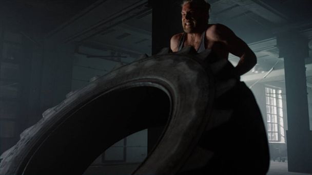 Силуэт крепкого человека, выполняющего силовые упражнения огромная шина. Сильный культурист - Фото, изображение