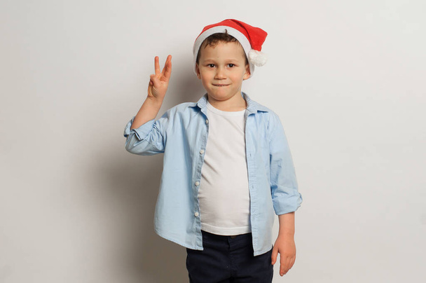 a boy wearing a santa claus hat shows three fingers - Photo, Image