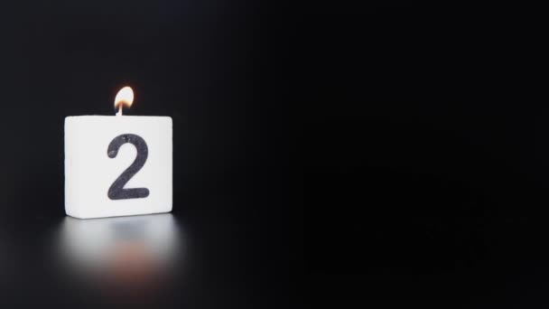 Uma vela quadrada dizendo que o número 2 está sendo aceso e apagado em um fundo escuro preto celebrando um aniversário ou aniversário - Filmagem, Vídeo