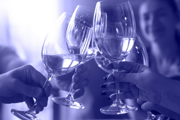Gruppe von Freunden bei einem Drink am Abend. Toast mit Weißwein in Nahaufnahme. Farbe des Jahres 2022, sehr peri - Foto, Bild