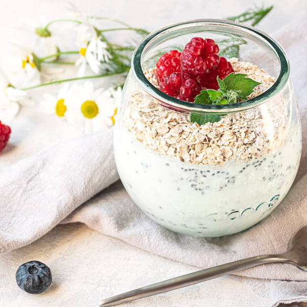 Un verre avec du yaourt en couches, des graines de chia, de l'avoine et des baies, servi au petit déjeuner - Photo, image