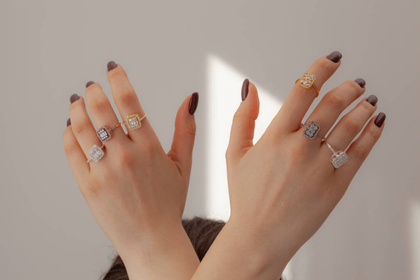 Diamentowe pierścienie na palcu damy z podniesionymi rękami przed szarym tłem. Kobieta pokazuje ręce na stylowe pierścienie palca. Koncepcja reklamy biżuterii - Zdjęcie, obraz