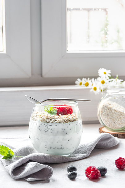 Een glas met gelaagde yoghurt, chia zaden, haver en bessen, geserveerd als ontbijt - Foto, afbeelding