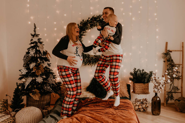 šťastná rodina v pyžamu s dětskými rodiči si hrát s dítětem skákání na posteli v ložnici. nový rok rodinné oblečení vypadá oblečení. Valentýnské slavnostní dárky - Fotografie, Obrázek