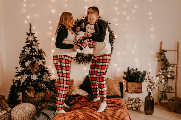 familia feliz en pijama con niñospadres juegan con el niño saltando en la cama en el dormitorio. ropa de la familia del año nuevo se ve trajes. Regalos de celebración del día de San Valentín - Foto, Imagen