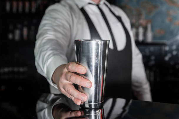 The hand of a professional bartender takes a tool for cooking and mixing alcoholic cocktail shaker, close-up. - Photo, Image