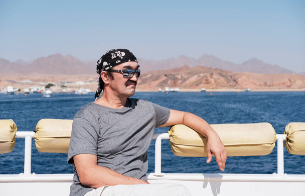 Feliz hombre asiático senior en gafas de sol y bandana viajando en barco en el mar. - Foto, imagen