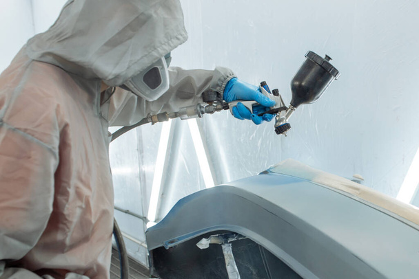 reparador de automóviles pintor mano en guante protector con pulverizador de aerografo pintura carrocería del coche en la cámara de pintura
. - Foto, imagen