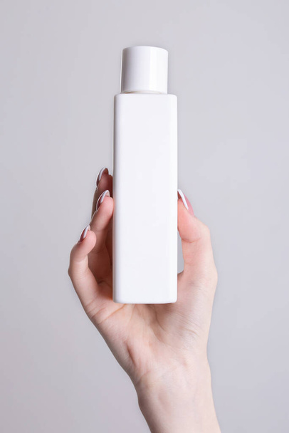 witte fles voor cosmetica in de hand van een vrouw. - Foto, afbeelding
