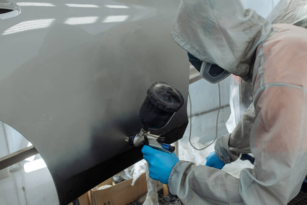 Professional car painter is painting in garage by airbrush. - 写真・画像