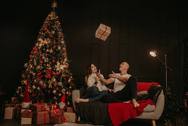 άντρας και γυναίκα ζευγάρι ερωτευμένοι ανοιχτά κουτιά δώρου λύστε ένα τόξο κοντά στο χριστουγεννιάτικο δέντρο - Φωτογραφία, εικόνα