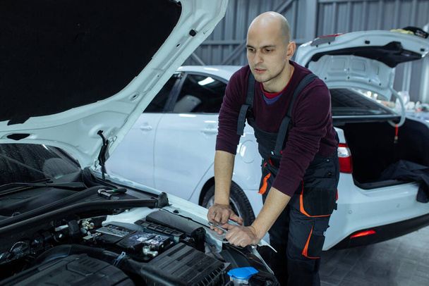 Un automóvil masculino está inspeccionando el motor de los autos. Servicio de coches y reparación de automóviles - Foto, imagen
