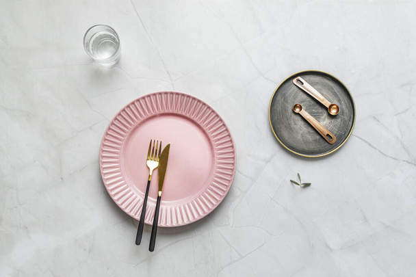 Pink plate with golden cutlery and vintage plate with measuring spoons and glass full of water on white marble table - Фото, изображение