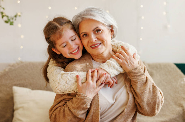 Cute happy little girl granddaughter hugging delighted elderly grandmother during Christmas holidays - Zdjęcie, obraz