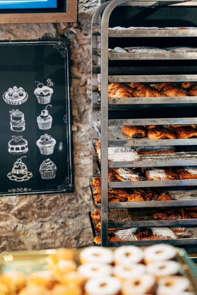 Bollos dulces espolvoreados con azúcar en polvo se encuentran en los estantes de una pastelería - Foto, Imagen