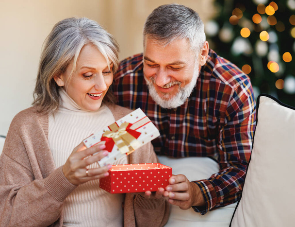 Amar marido hombre mayor dando regalo de Navidad caja de regalo a feliz esposa sorprendida - Foto, Imagen