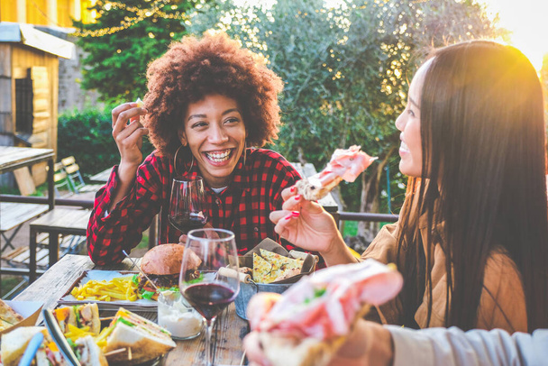 Grupo de amigos multiétnicos vivendo um estilo de vida saudável e sorrindo e brincando enquanto bebe vinho tinto no restaurante pub ao ar livre - Jovens brindam com copo de vinho durante a happy hour no bar - Foto, Imagem