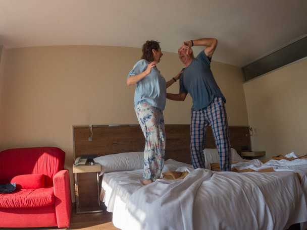 Love lives forever! Older couple in a hotel. Older man and woman enjoy spending time together. Have fun and jump on the bed. - Photo, Image
