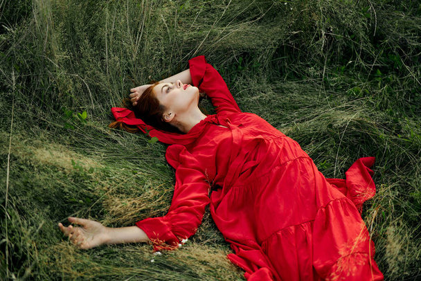 woman in red dress lies on the grass in the field nature landscape - Фото, зображення