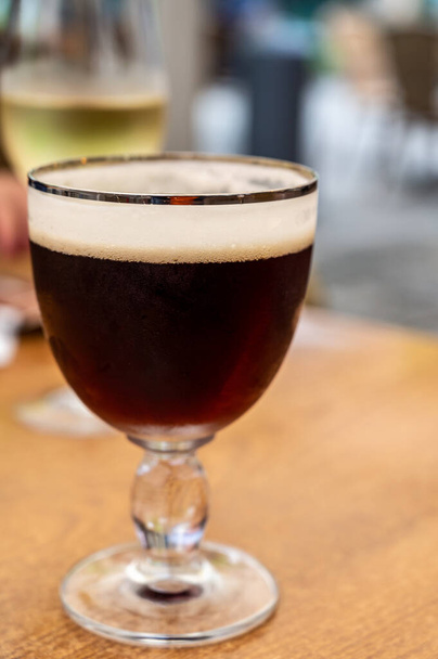 Стакан тёмного вкусного бельгийского дуббл-коричневого пива с пивоварни аббатства подается на открытом воздухе. - Фото, изображение