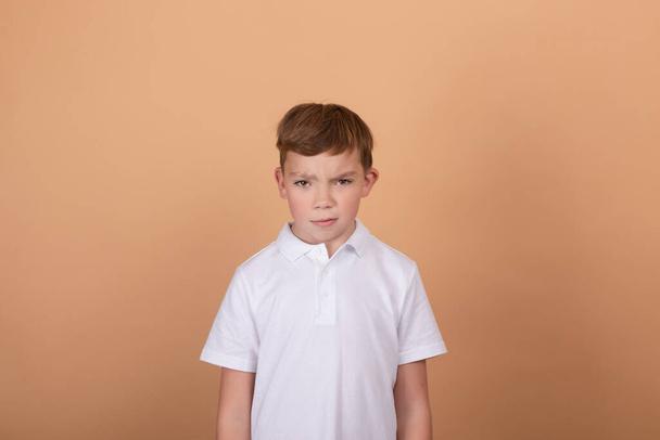 érzelmi portré egy tinédzser fiúról. elbűvölő iskolás fiú. Gyönyörű gyerek. világosbarna háttér - Fotó, kép