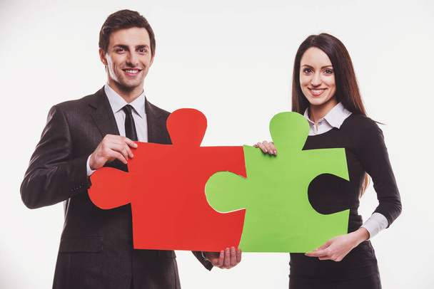 Two successful young business people in formal wear trying to connect pieces of puzzle. - Foto, imagen