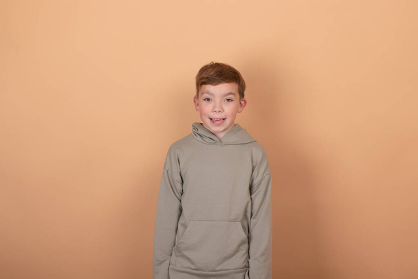 Knappe jonge Europese jongen tiener die naar de camera kijkt, met casual groene hoodie geïsoleerd op bruine achtergrond. kopieer vrije ruimte voor tekst - Foto, afbeelding