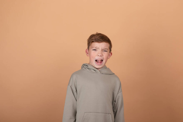 Knappe jonge Europese jongen tiener die naar de camera kijkt, met casual groene hoodie geïsoleerd op bruine achtergrond. kopieer vrije ruimte voor tekst - Foto, afbeelding