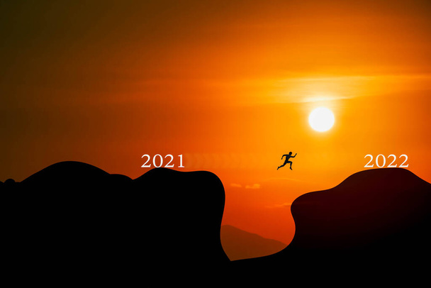 Concept Début de la nouvelle année. Bonne année 2022. Les lettres blanches 2021 passent à 2022 sur une montagne avec la lumière du coucher du soleil et les gens sautent. Fond flou. - Photo, image