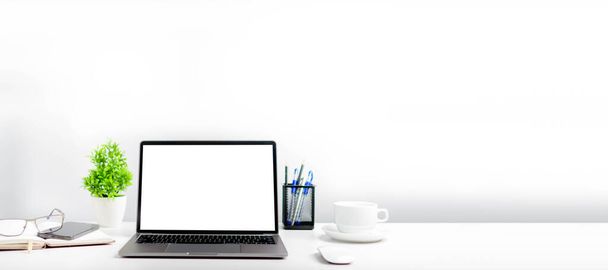 Blanco witte scherm laptop op een witte tafel in het kantoor. Een werkend concept met behulp van technologie, notebook, smartphones, apparaten. Kopieer ruimte aan de rechterkant voor ontwerp of tekst, Close-up, grijs en wazig achtergrond - Foto, afbeelding