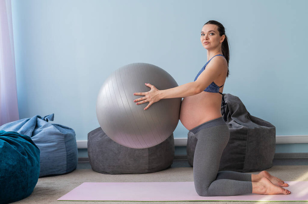 Pregnant european woman performs exercises with fitness ball. Expectant mother is doing yoga in the 3rd trimester. Girl in the classroom in preparation for childbirth. - Foto, immagini
