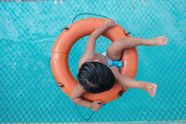 小さな男の子の上に横たわる水泳プールの青い水の野外活動にリングを泳ぐ - 写真・画像