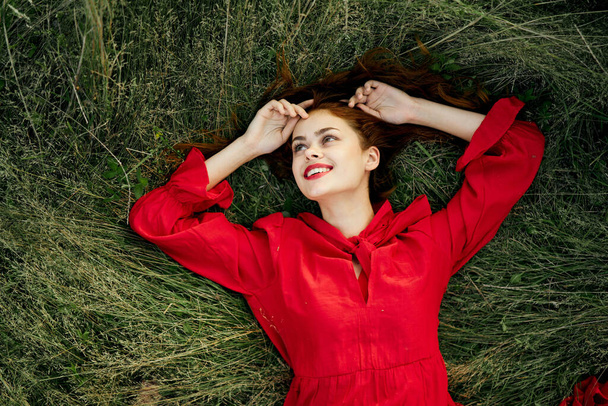 cheerful woman in a red dress lies on the grass top view - Fotografie, Obrázek