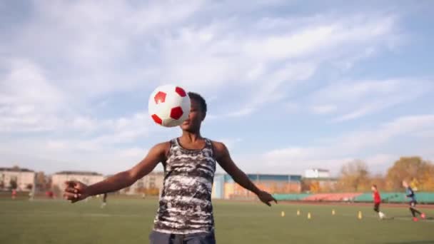 Chica negra joven en el entrenamiento de fútbol hace malabares con la pelota y la lanza de una rodilla a otra. Concepto de deporte y estilo de vida activo - Metraje, vídeo