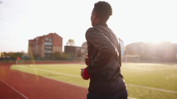 Молодая чёрная женщина в спортивной форме бежит по беговой дорожке городского стадиона. Вид сзади. Медленное движение - Кадры, видео