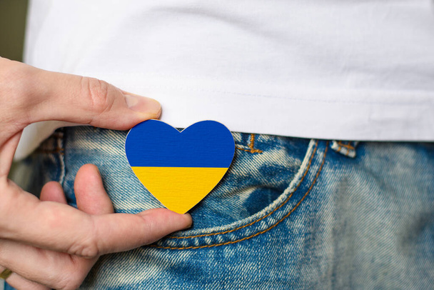 Patriot van Oekraïne! Houten badge met de vlag van Oekraïne in de vorm van een hart in de hand van een man. Nationale feestdag van Oekraïne. - Foto, afbeelding