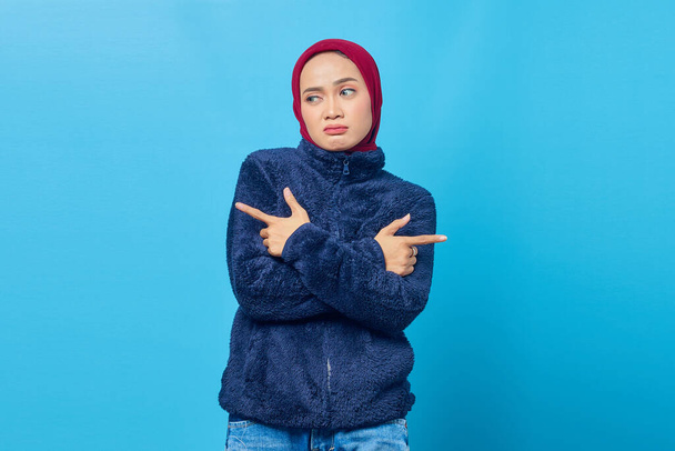 Confused young Asian woman pointing sideways and looking sideways on blue background - Φωτογραφία, εικόνα