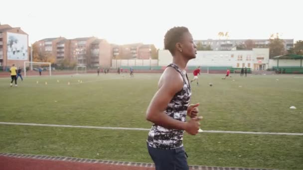 Mladá Afroameričanka běhá na běžeckém pásu městského stadionu během tréninku fotbalového týmu. Zpomalený pohyb - Záběry, video