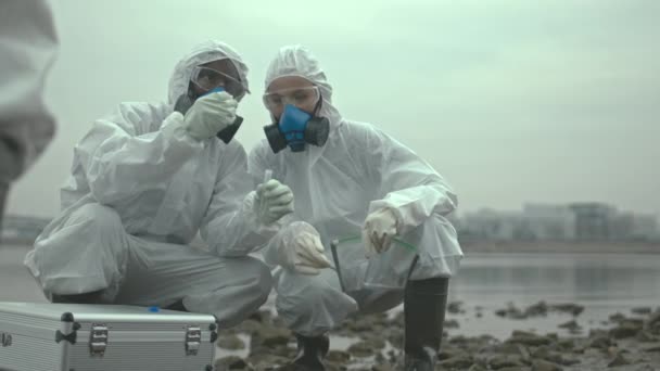 Lento disparo de equipo de científicos en trajes químicos y máscaras respiratorias tomando muestras de suelo en tubo de ensayo examinando el territorio de riesgo biológico donde ha ocurrido la catástrofe ecológica - Imágenes, Vídeo