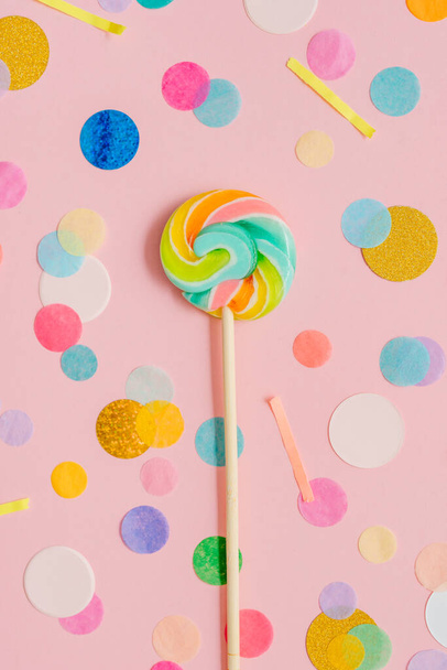 Multicolored lollypop on the pink background with confetti. Top view, flat lay. - Foto, Imagem