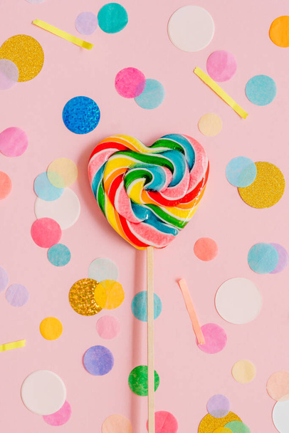 Multicolored heart shape lollypop on the pink background with confetti. valentine's day concept. Top view, flat lay. - Foto, imagen