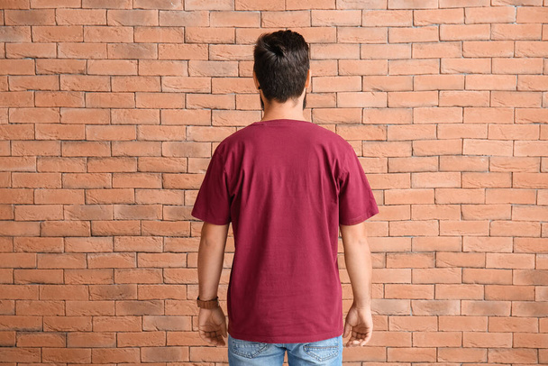 Όμορφος άντρας με κόκκινο μπλουζάκι σε φόντο από τούβλα. - Φωτογραφία, εικόνα