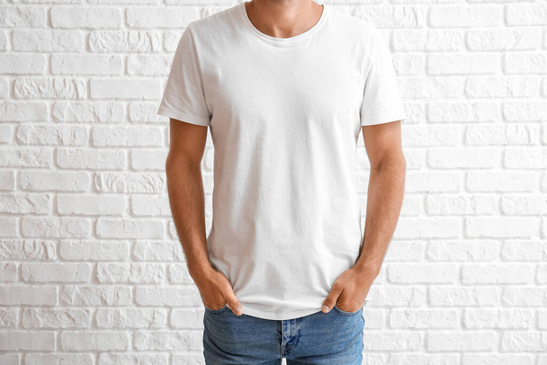 Красивый молодой человек в стильной футболке на белом кирпичном фоне - Фото, изображение
