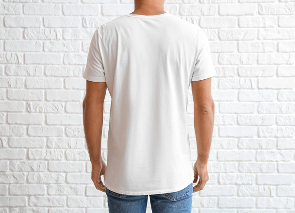 Красивый молодой человек в стильной футболке на белом кирпичном фоне, вид сзади - Фото, изображение
