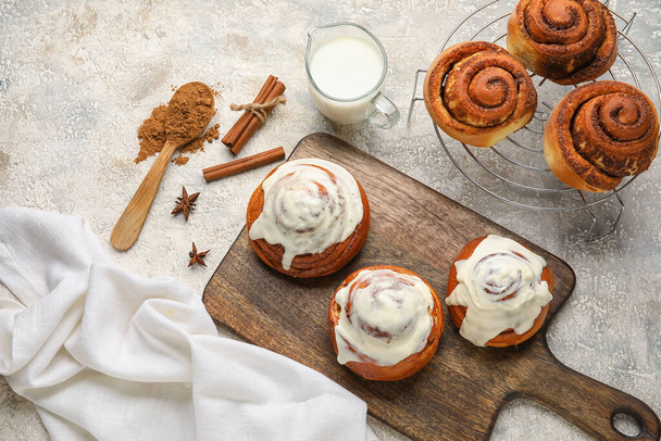 Wooden board and grid with tasty cinnamon rolls on light background - Foto, Imagem